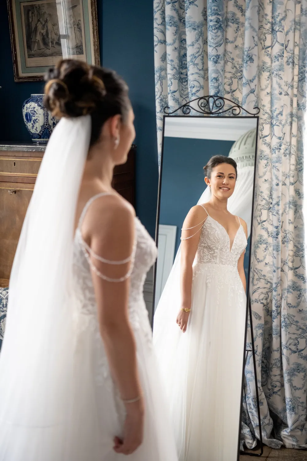 La mariée se regarde dans un grand miroir, en robe et voile