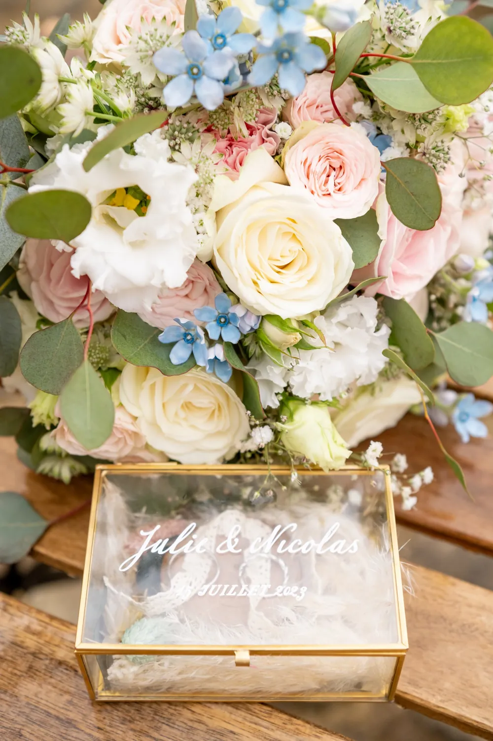 Le bouquet de roses pastel posé près de la boîte des alliances gravée